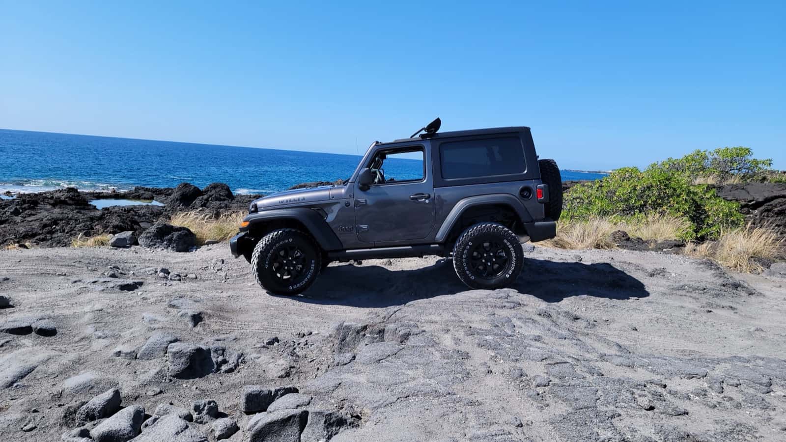 Gray two-door Jeep Wrangler on a lava shoreline above the ocean